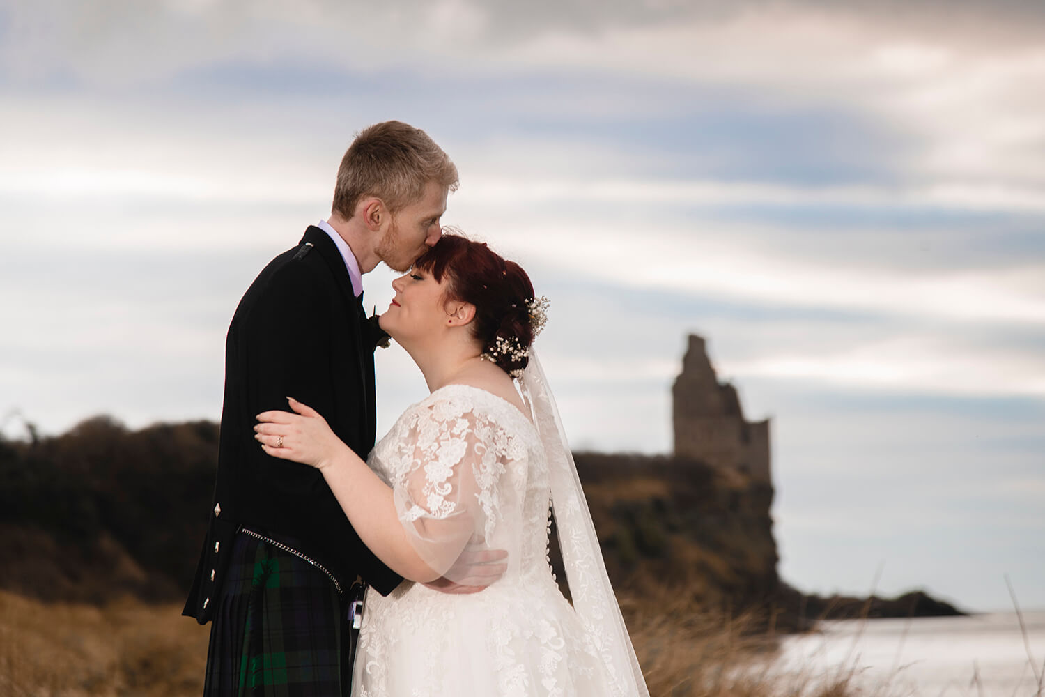 Bride and groom standing and embracing with view of Greenan Castle in the backgroud by Ayrshire weding photographer Richard Campbell