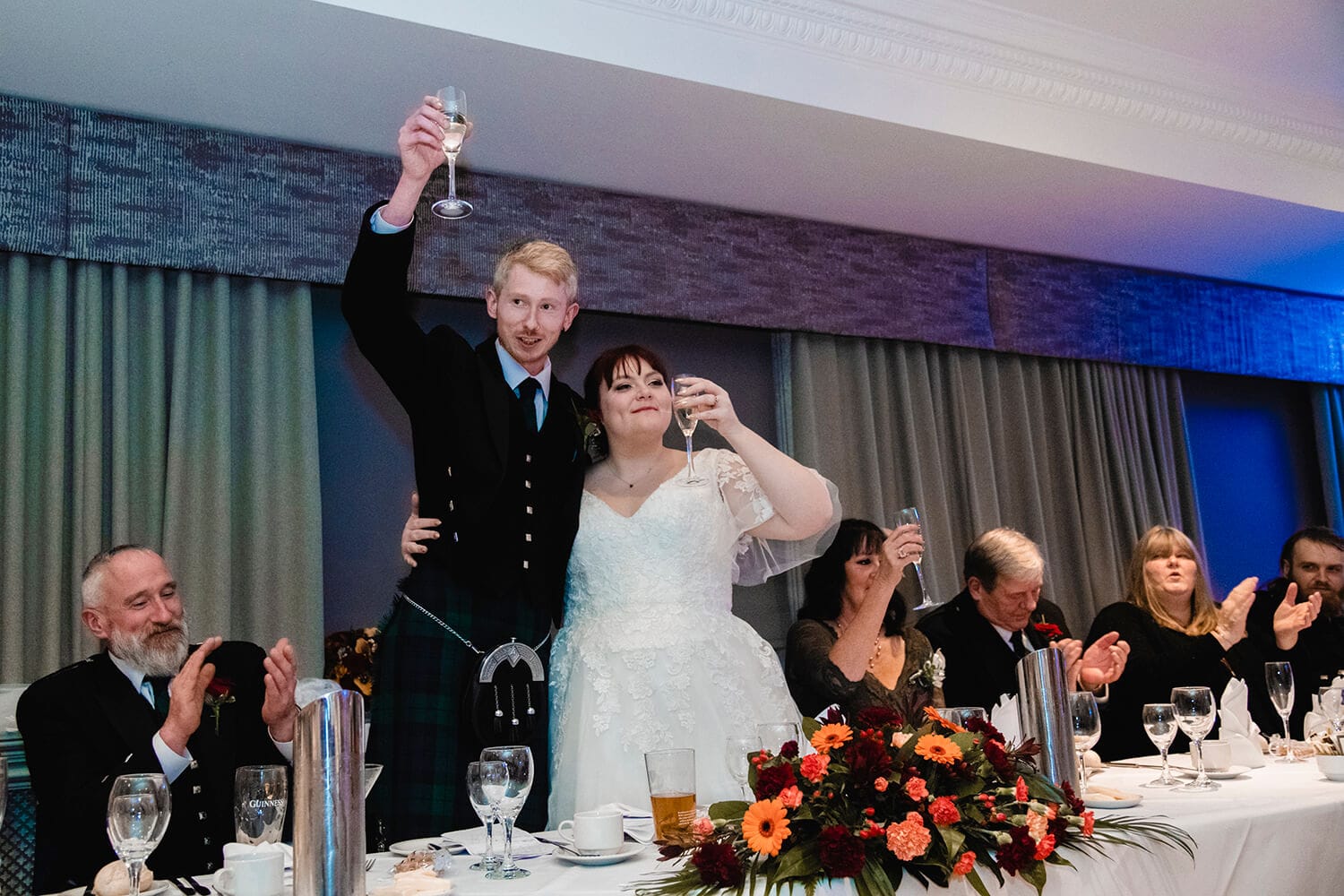 Bride and groom standing at top table and holding glasses aloat for toast at Fairfield Hotel in Ayr by Ayrshire wedding photographer Richard Campbell